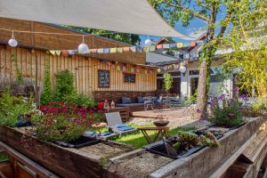Biergarten an einem schönen Sommertag, mit vielen Pflanzen und gemütlichen Sitzmöglichkeiten.