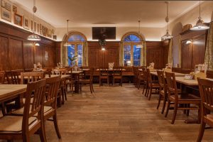 Gaststube von innen, mit Holzboden und bequemen Stühlen, gemütliche Beleuchtung und hoher Decke.