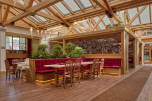 Unsere Gaststube Tante Paula mit viel warmem Holz und gemütlichem Licht und roten Sitzbezügen.