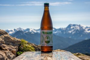 Selbstgebrautes Tante Paula Bier mit Bergpanorama im Hintergrund auf Berggipfel.