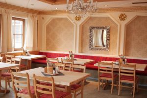 Gaststube von Tante Paula in Burgberg von innen mit roten Sitzpolstern, hellen Wänden in König Ludwig Stil gehalten, mit Kronleuchter und Spiegel.